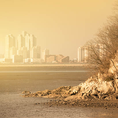 riva rocciosa, grattacieli di una città in lontananza, smog